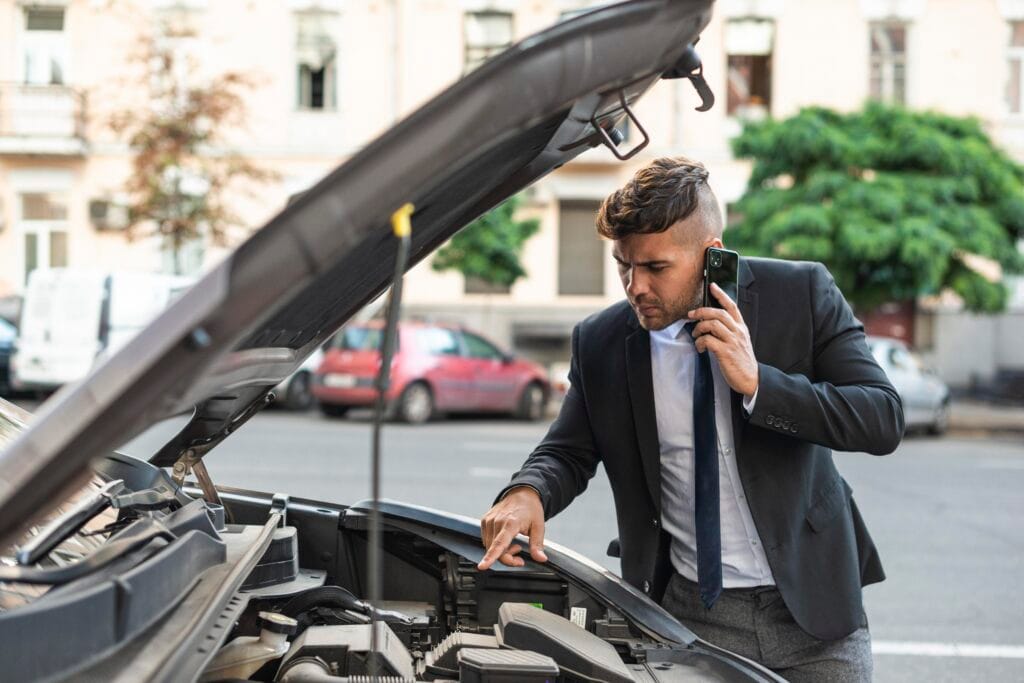 A man in a suit talks on a cell phone while examining the hood of a car.